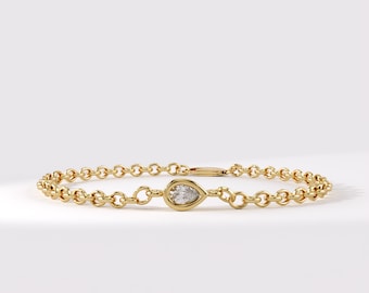 May include: A gold chain bracelet featuring a single pear-shaped diamond set in a gold bezel. The bracelet is constructed from a series of small, round, interlocking gold links that form a continuous circular band around the central gemstone.