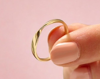 May include: A polished gold ring with a smooth, continuous band featuring a subtle, organic wave-like twist. The metal surface is reflective and uniform in color, showcasing a simple, rounded profile that maintains a consistent thickness throughout.