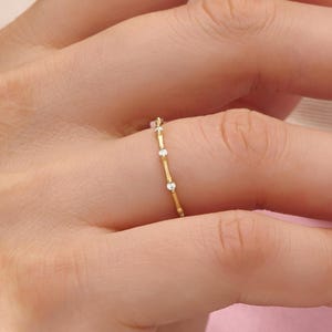 Puede incluir: Un delicado anillo de oro con un diseño lineal. El anillo presenta pequeñas piedras preciosas transparentes y detalles en forma de corazón. El anillo se lleva en un dedo, mostrando sus finos detalles y su estilo elegante.