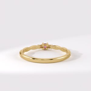 Pode incluir: Um anel de ouro com uma banda fina e polida, apresentando um design ondulado nas laterais. O centro do anel &eacute; cravejado com uma pequena pedra preciosa redonda de cor rosa vibrante, mantida no lugar por uma crava&ccedil;&atilde;o simples de quatro garras.