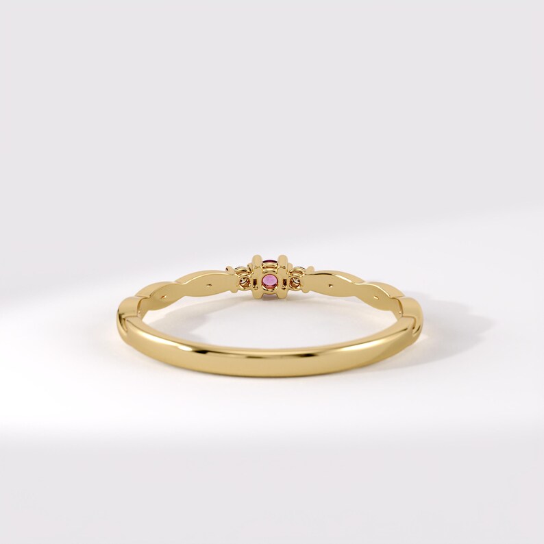 Pode incluir: Um anel de ouro com uma banda fina e polida, apresentando um design ondulado nas laterais. O centro do anel &eacute; cravejado com uma pequena pedra preciosa redonda de cor rosa vibrante, mantida no lugar por uma crava&ccedil;&atilde;o simples de quatro garras.