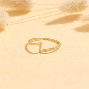 May include: A gold ring featuring a V-shaped design. The ring is slender and elegant, with the inscription "LUCY'S 14K" on the band. The background is a soft, neutral colour.