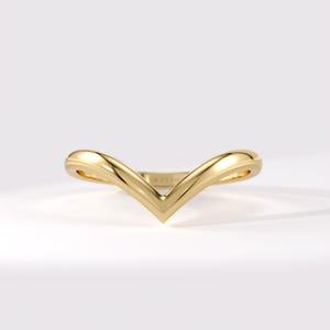 Pode incluir: Um anel de ouro amarelo polido com um design liso em forma de V ou chevron. A banda tem um perfil arredondado e um acabamento metálico sólido e contínuo que se estreita até um ponto no centro, criando uma silhueta limpa e simétrica.