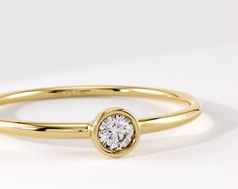 May include: A yellow gold ring featuring a single round brilliant-cut diamond set in a smooth bezel setting. The band is thin and polished, with the inscription LUCY 14K visible on the inner surface of the gold band near the diamond setting.
