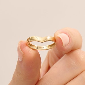 Pode incluir: Um anel dourado com um design em forma de V. O anel é segurado entre dois dedos. O interior do anel tem o texto "LUCYS 14K".