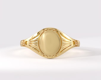 May include: A polished gold-tone signet ring featuring a smooth, oval-shaped center plate. The band displays decorative grooved lines radiating from the central oval, with small circular indentations along the sides of the ring shank.