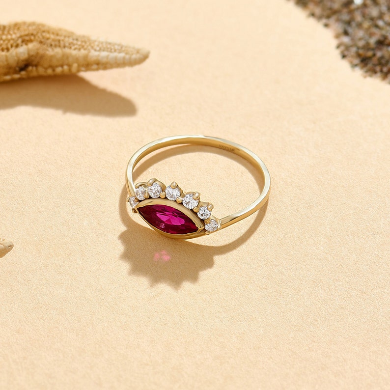 May include: A gold ring with a marquise-shaped ruby gemstone surrounded by a halo of smaller white gemstones.