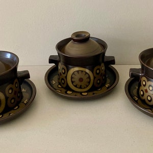 May include: Three brown ceramic soup bowls with lids and matching saucers. Each bowl has a dark brown exterior with a floral pattern in yellow and red. The lids have a small handle.