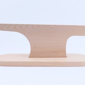 Könnte beinhalten: Ein Holzständer mit einer geschwungenen Oberseite und einer flachen Basis. Der Ständer ist aus hellem Holz gefertigt und hat eine glatte Oberfläche.