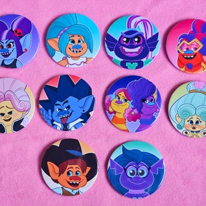 May include: Ten round, colorful buttons featuring characters from the animated movie Trolls World Tour. The buttons feature various characters, including Poppy, Branch, Barb, and Biggie.