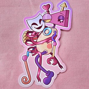 May include: A whimsical sticker featuring a cartoon character with a mask, a box-shaped head with an arrow, and a spotted body. The character is wrapped in pink ribbons and holds a staff. The sticker has a pink border and is set against a pink background.