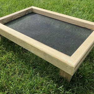 May include: A wooden bird feeder with a raised platform and a wire mesh bottom. The feeder is light brown and has a rustic look.