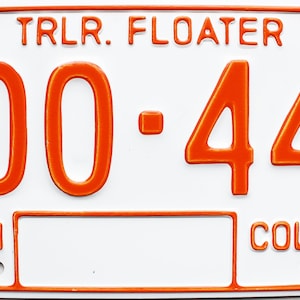 May include: A white trailer license plate with orange text. The plate reads "TRLR. FLOATER 86 300-447 BRITISH COLUMBIA".