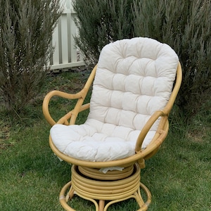 Peut inclure: Un fauteuil en rotin pivotant avec un coussin blanc. Le fauteuil a une base ronde et est fait de mat&eacute;riaux naturels.