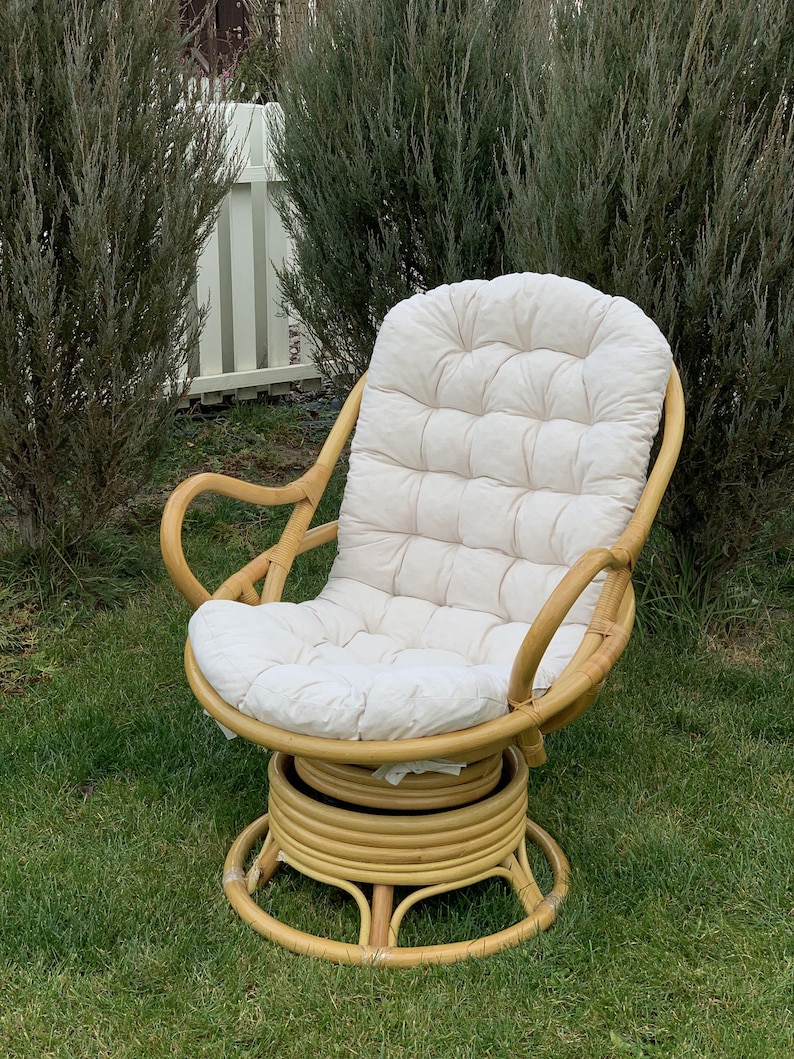 Peut inclure: Un fauteuil en rotin pivotant avec un coussin blanc. Le fauteuil a une base ronde et est fait de mat&eacute;riaux naturels.