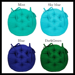 May include: Four round chair cushions in different colours: mint green, sky blue, blue, and dark green. Each cushion has a tied bow and a buttoned design.