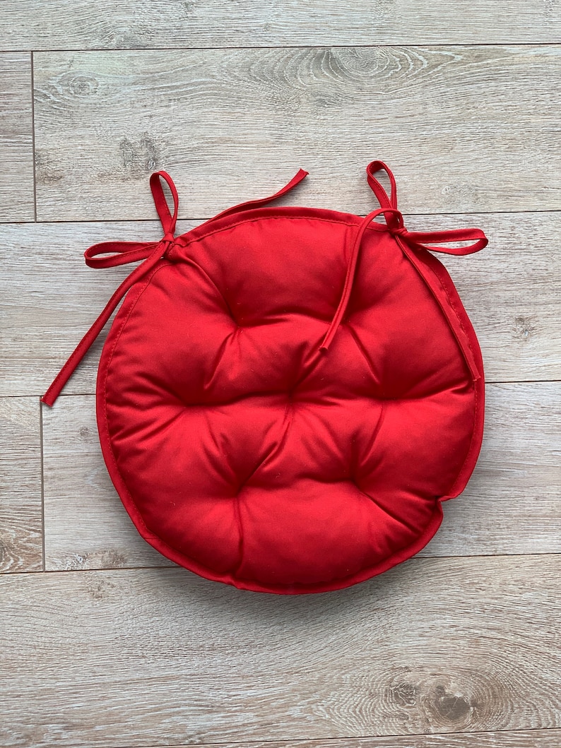 May include: Red round chair cushion with a tufted design and ties for attaching to a chair.