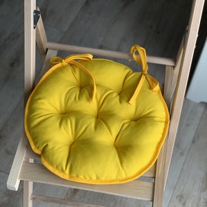 May include: A bright yellow round chair cushion with a tufted design and ties to attach it to a chair.