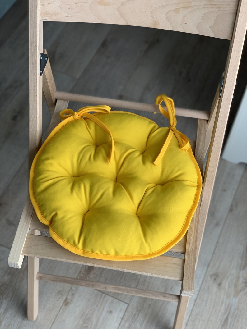 May include: A bright yellow round chair cushion with a tufted design and ties to attach it to a chair.