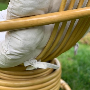 Peut inclure: Une chaise en rotin tress&eacute; avec un coussin blanc. La chaise a un dossier arrondi et une base circulaire.