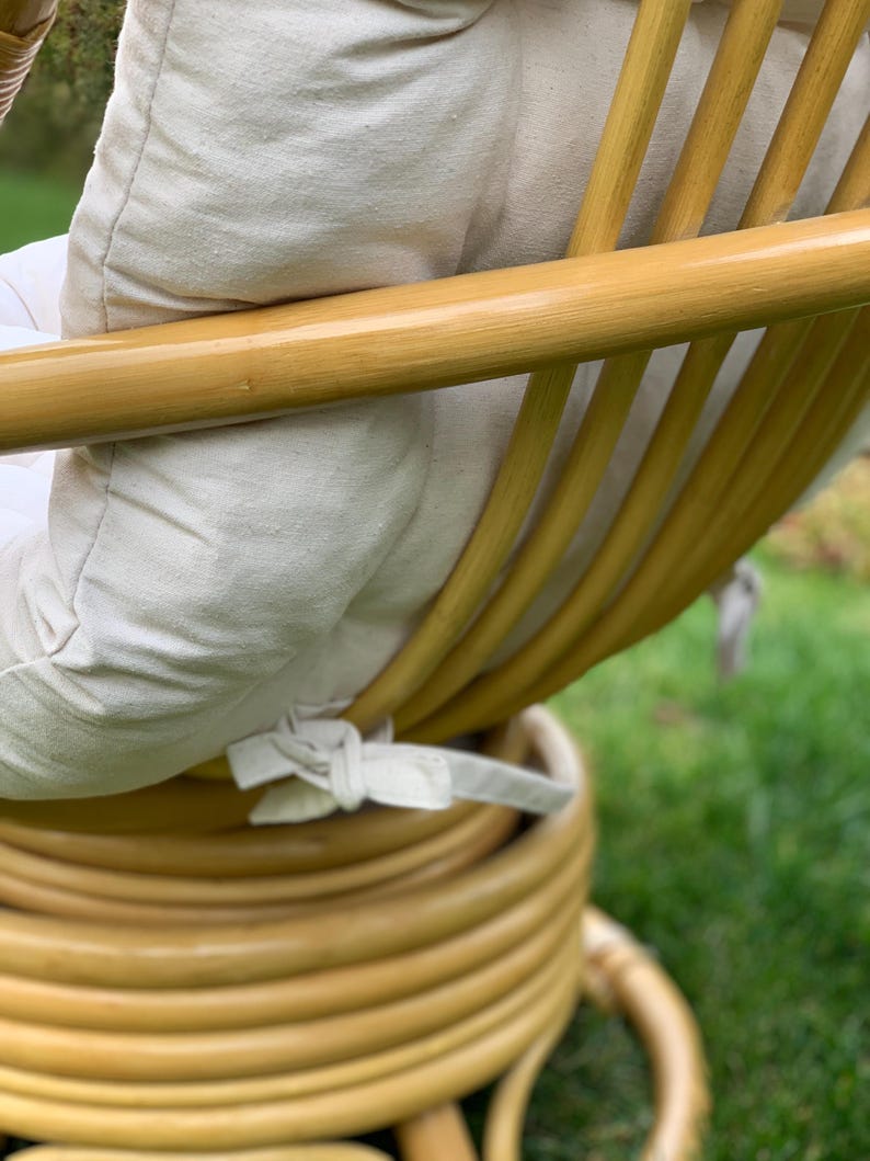 Peut inclure: Une chaise en rotin tress&eacute; avec un coussin blanc. La chaise a un dossier arrondi et une base circulaire.
