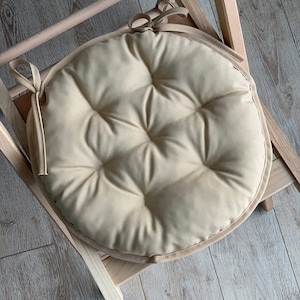 May include: A beige round chair cushion with a tufted design and a tied bow on the side.