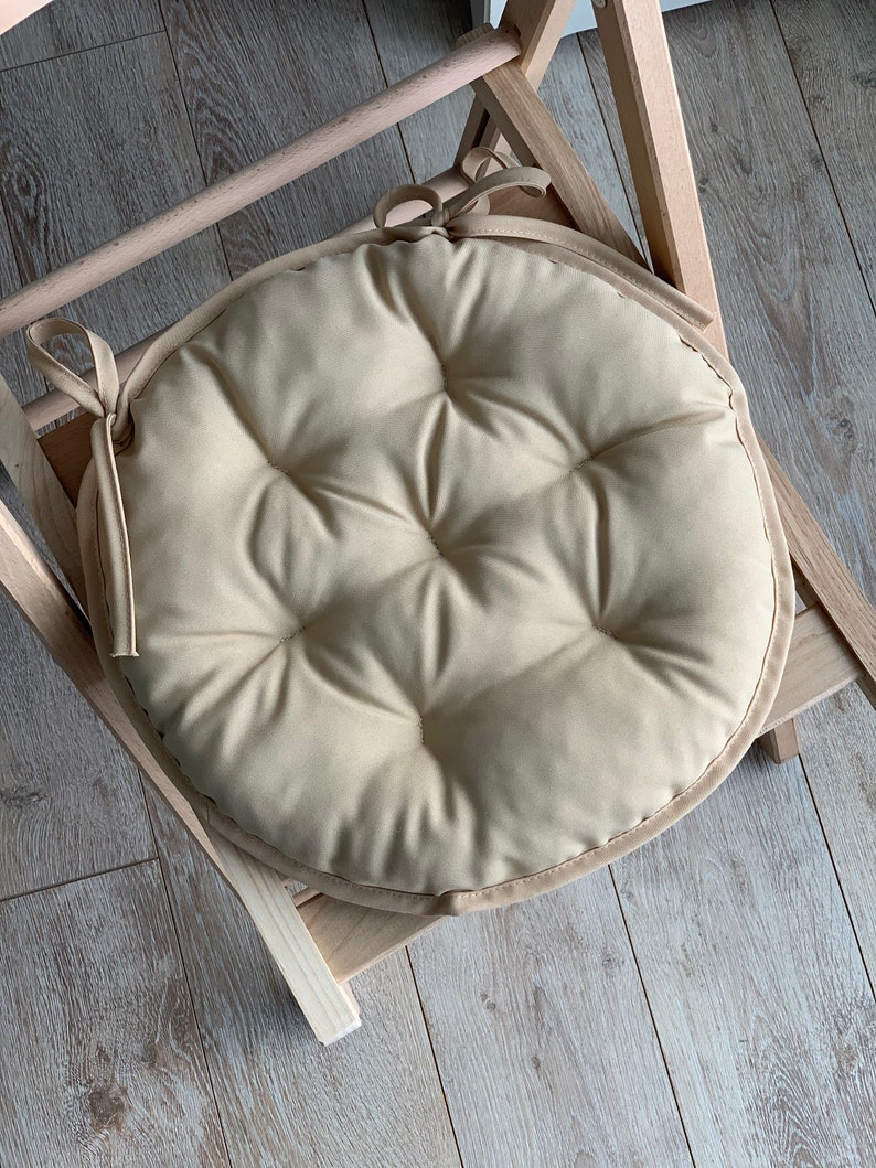 May include: A beige round chair cushion with a tufted design and a tied bow on the side.