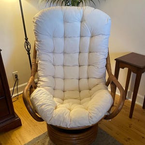 Peut inclure: Un fauteuil pivotant avec un coussin rembourr&eacute; blanc et une structure en osier brun. Le fauteuil est pos&eacute; sur un sol en bois avec un tapis en dessous.