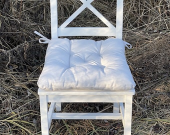 Puede incluir: Silla de madera blanca con un cojín blanco. La silla tiene un diseño sencillo con un respaldo en forma de cruz.