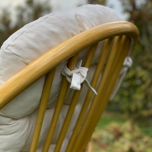 Peut inclure: Gros plan de l'arri&egrave;re d'un fauteuil en osier brun clair avec un coussin blanc. Le fauteuil a un dossier incurv&eacute; et un design tiss&eacute;. Le coussin est attach&eacute; au fauteuil avec des liens en tissu blanc.