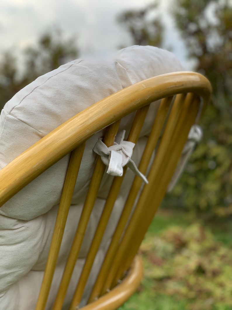 Peut inclure: Gros plan de l'arri&egrave;re d'un fauteuil en osier brun clair avec un coussin blanc. Le fauteuil a un dossier incurv&eacute; et un design tiss&eacute;. Le coussin est attach&eacute; au fauteuil avec des liens en tissu blanc.
