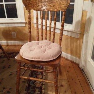 May include: A wooden chair with a carved back and a light pink cushion. The chair is sitting on a patterned rug in front of a window.