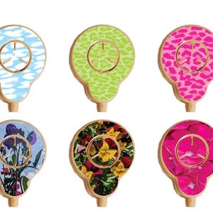 May include: Six different designs of round, colorful stickers for a smart watch. The stickers feature a variety of patterns, including clouds, leopard print, flowers, and abstract designs. The stickers are designed to be placed on the face of a smart watch.