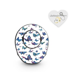 Puede incluir: Una pegatina redonda blanca con un patrón de mariposa colorido. La pegatina está diseñada para adaptarse a un objeto pequeño y redondo, como una botella de agua o una funda de teléfono.