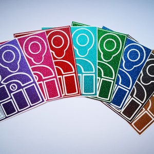 Könnte beinhalten: Ein Set rechteckiger Glitzeraufkleber in Fächerform in den Farben Violett, Pink, Rot, Türkis, Grün, Blau, Schwarz und Gold. Jeder Aufkleber zeigt die weiße Umrisszeichnung eines medizinischen Geräts und enthält kleingedruckten Text.