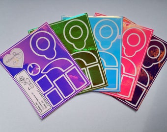 Puede incluir: Cinco hojas de pegatinas iridiscentes con diferentes fondos de color y contornos blancos de varias formas, incluyendo un corazón, un círculo y una luna creciente. El texto "Pegatinas personalizables" está impreso en la hoja morada.