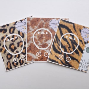 May include: Four different patterned stickers with a white outline of a cartoon face. The stickers have a leopard print, a brown and white fur print, a tiger print, and a brown and white fur print. The stickers have the text "BeAmelia Stickers" and "Available Here: Etsy.com/shop/BeAmelia Stickers" on them.
