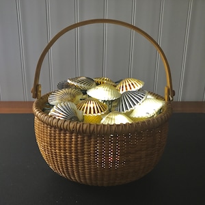 May include: A woven basket with a handle filled with white, brown, and gray seashells. The shells are lit from within, creating a warm glow.