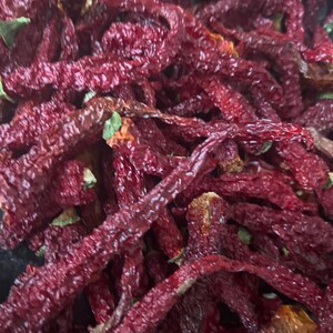 May include: A close-up of a pile of dried red chili peppers. The peppers are long and thin, and they have a deep red color.