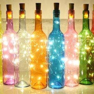 May include: Eight glass bottles with cork tops, each containing a string of white LED lights. The bottles are in various colours: yellow, pink, clear, orange, blue, and green.