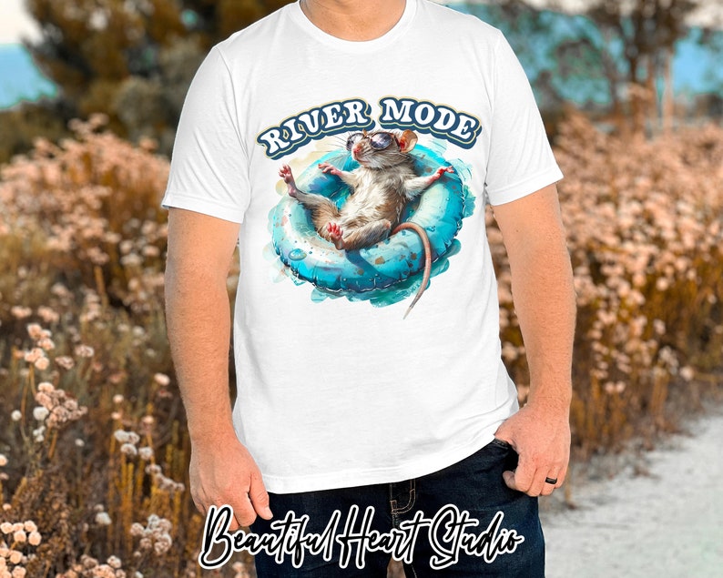 Puede incluir: Camiseta blanca con un gr&aacute;fico de una rata con gafas de sol flotando en un flotador inflable azul. El texto "River Mode" est&aacute; impreso en amarillo sobre la rata.