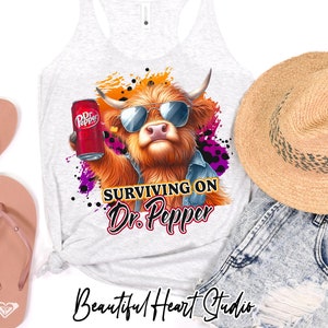 May include: A white tank top featuring a graphic of a Highland cow wearing sunglasses and holding a can of Dr Pepper. The text "Surviving on Dr. Pepper" is beneath the cow. The tank top is displayed against a white backdrop.