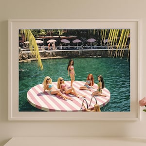 May include: A framed print showing dolls in swimwear on a striped floating platform in a pool. The image has a retro aesthetic, with a clear turquoise pool and a vintage summer vacation theme. The dolls are the focal point.