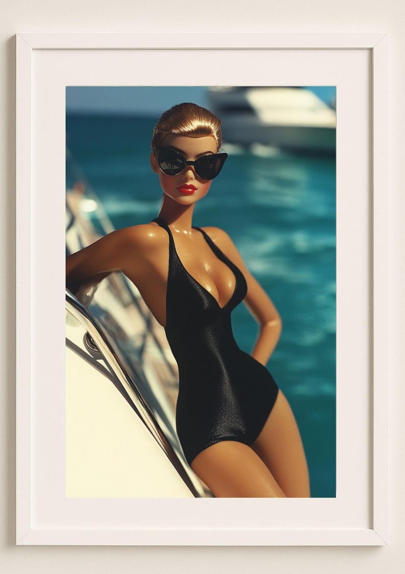 May include: A framed print featuring a doll in a black swimsuit and sunglasses, posing on a yacht. The doll has red lipstick and blonde hair. The background shows blue water and a boat.