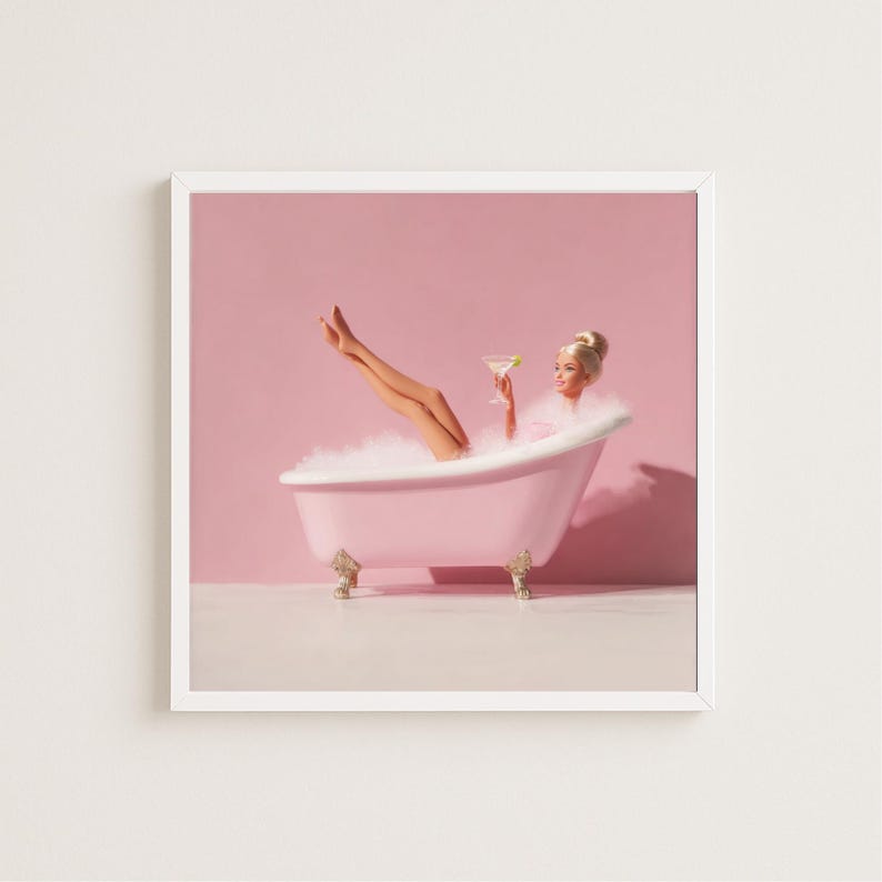 May include: A framed print featuring a woman relaxing in a pink clawfoot bathtub filled with bubbles. She holds a cocktail and has her legs raised. The background is a solid pink color.