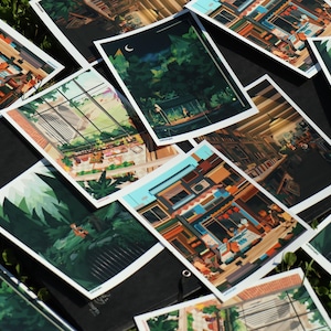 May include: A collection of colourful illustrated prints featuring various scenes, including a cityscape, a forest, and a building with a shop front. The prints are arranged on a black surface and surrounded by green grass.