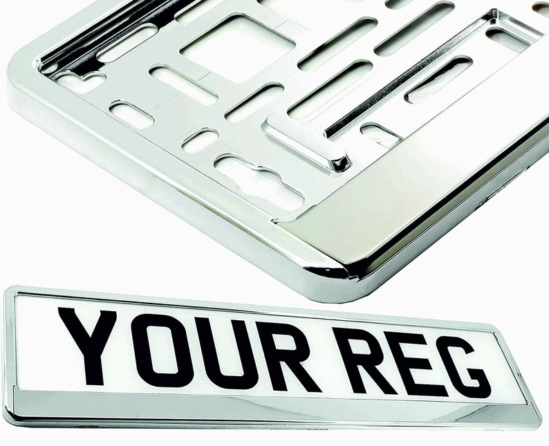 May include: A chrome license plate frame and a license plate with the text "YOUR REG" in black. The frame is rectangular with a shiny, reflective surface. The license plate is white with black lettering.