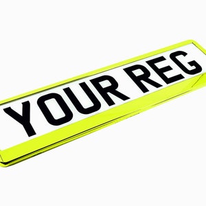 May include: A rectangular license plate with the text "YOUR REG" in bold black letters on a white background. The plate is encased in a bright yellow frame, creating a striking contrast against the white background.