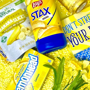 May include: A yellow and blue bag of Lay's Stax Original potato chips, a yellow bag of freeze-dried banana slices, a yellow box of Lemonhead candy, and a yellow sign that says "Don't stress your yes" with yellow and blue polka dots in the background.