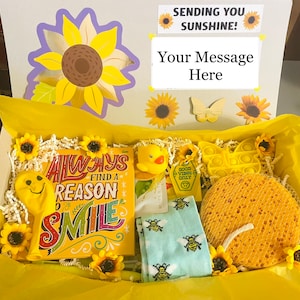 May include: A yellow gift box filled with yellow themed items, including a yellow smiley face balloon, a yellow bath sponge, a yellow pop-it toy, a yellow rubber duck, and a card with the text "Always find a reason to smile".